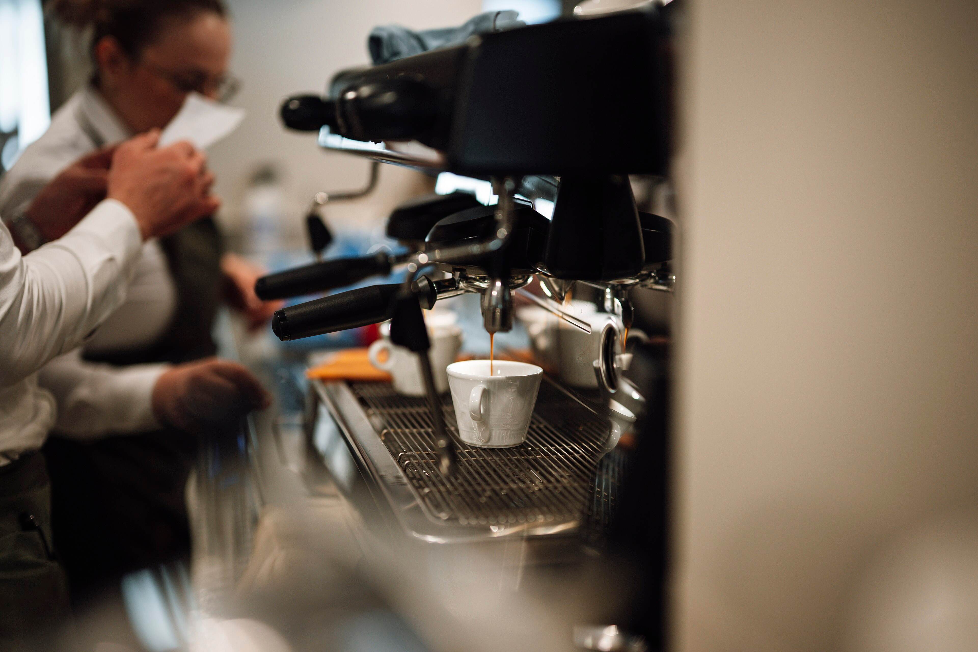 A barista at work behind a busy café counter while customers wait
