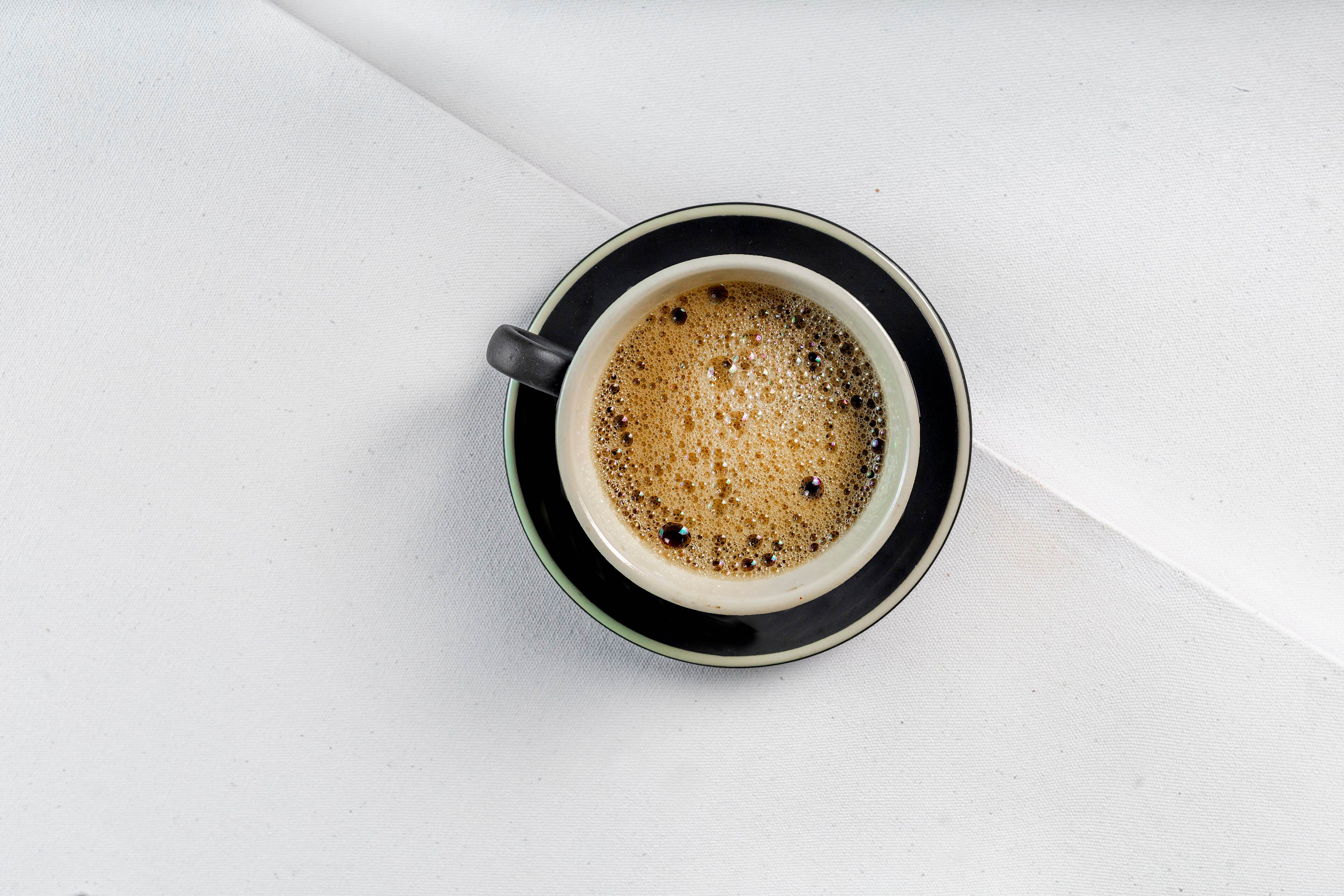 Top-down view of a black coffee in a dark cup on a white surface