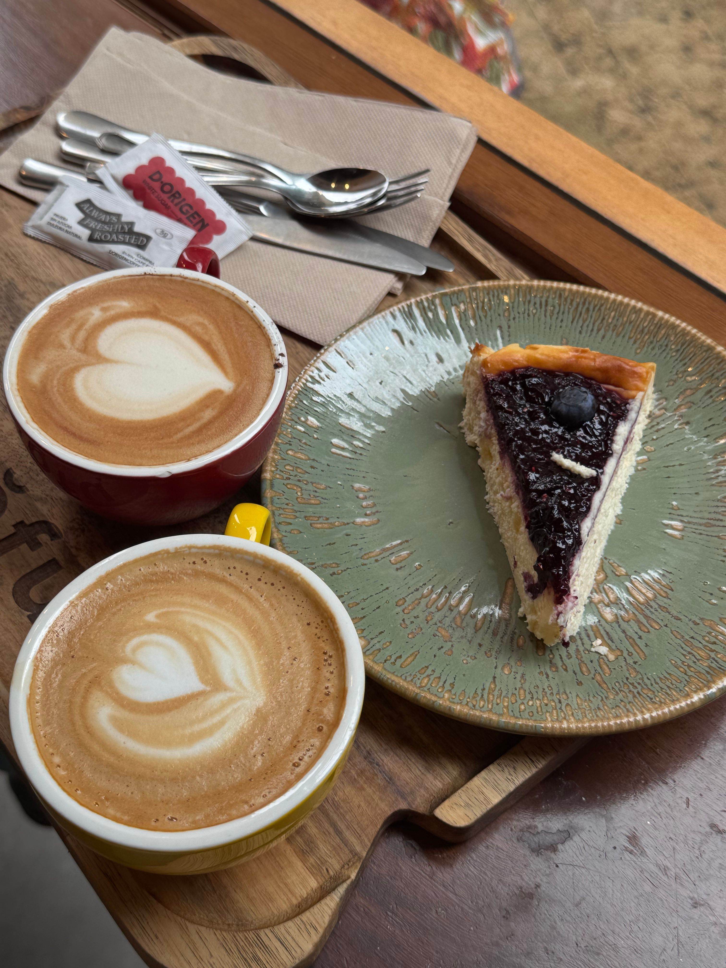 Two cappuccinos with heart latte art shared over slices of cheesecake
